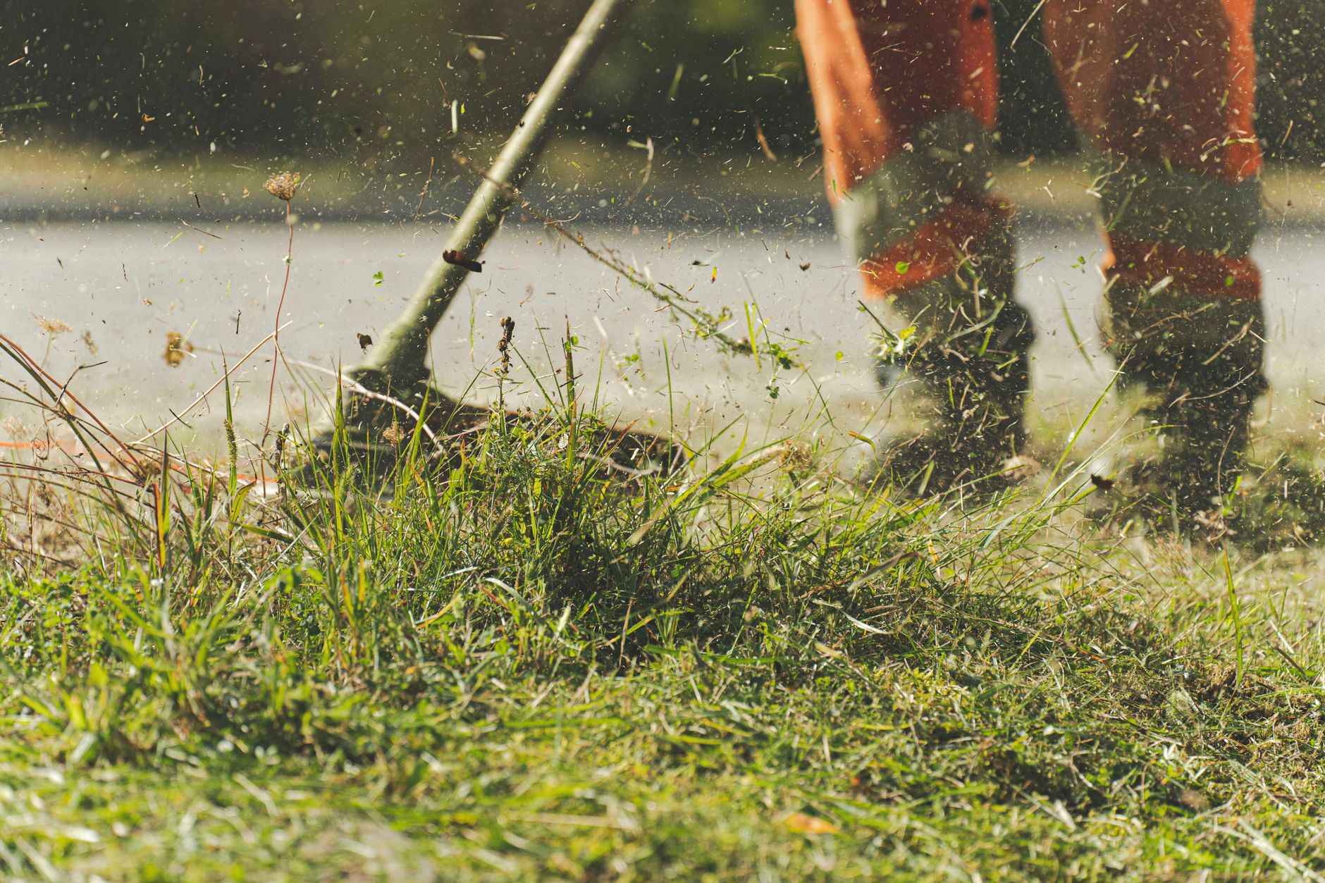 A worker in high-visibility trousers edging grass with a line trimmer beside a path